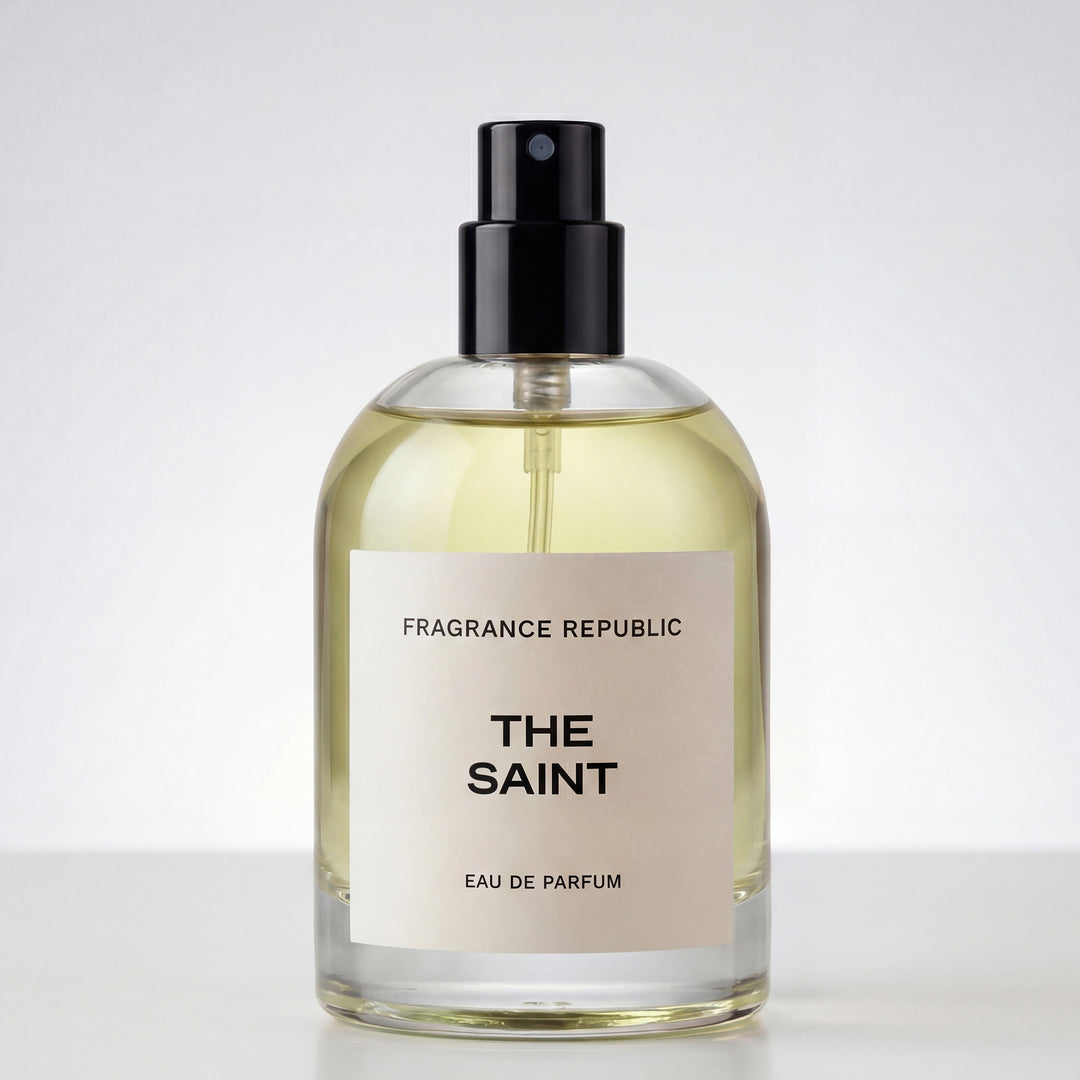 Clear glass bottle of THE SAINT eau de parfum with black spray cap on white background